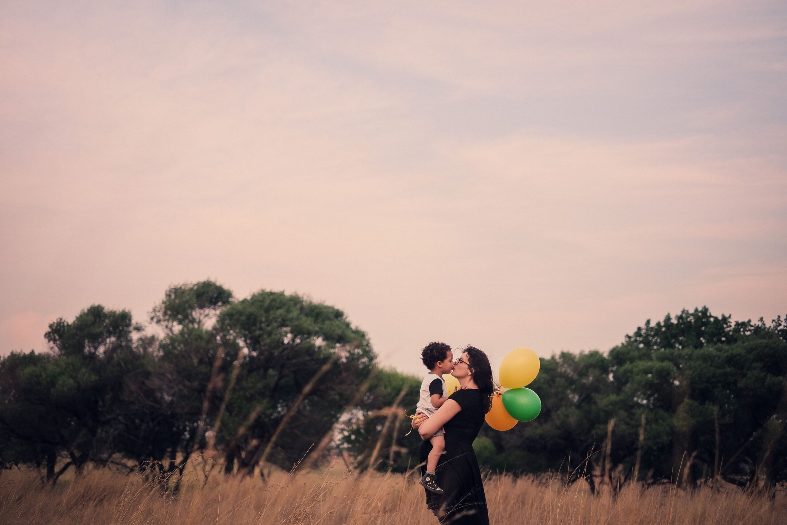 A mother holding a child in a parkland with balloons